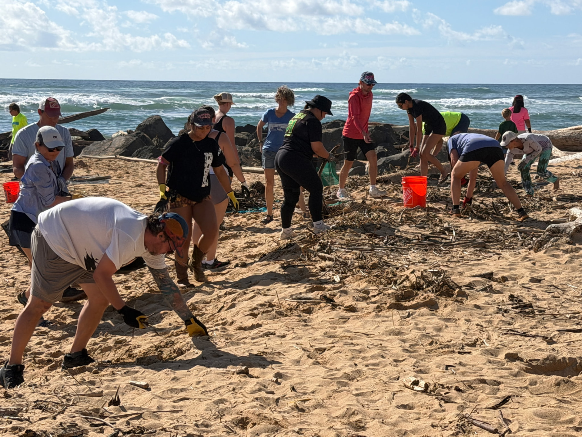 Volunteers work the shoreline near the rock groin, filling buckets with storm debris pulled from the sand.